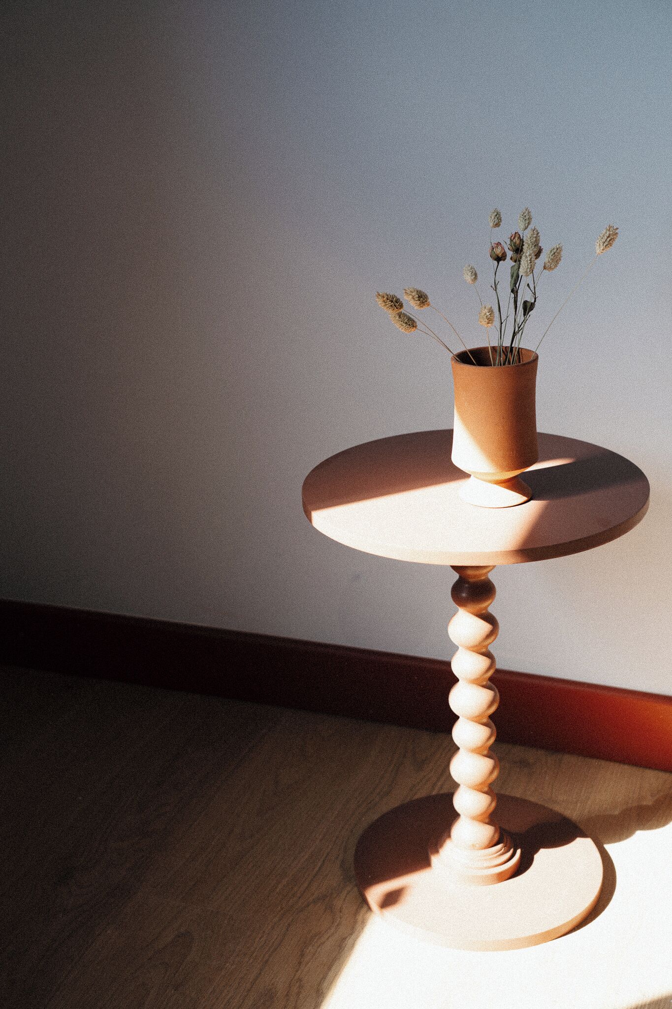 A round wooden table with a vase of dried flowers on top.