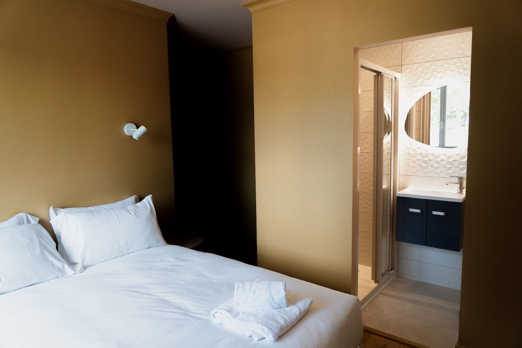 A hotel room with a bed, a wall-mounted light, and a bathroom visible through an open door.