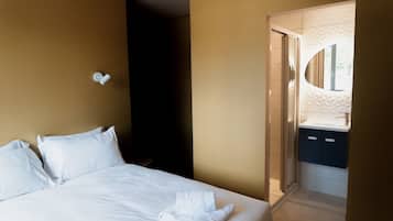 Une chambre d’hôtel avec un lit, une lampe fixée au mur et une salle de bain visible à travers une porte ouverte.