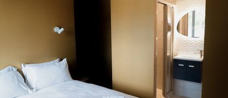 Hotellihuone, jossa on sänky, seinään kiinnitetty valaisin ja kylpyhuone, joka näkyy avoimesta ovesta.