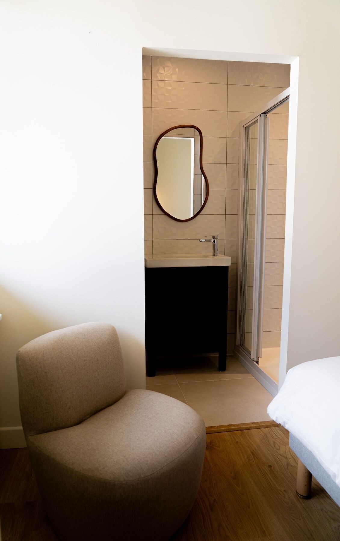 A compact hotel room with a round chair, a small sink, and a mirror.
