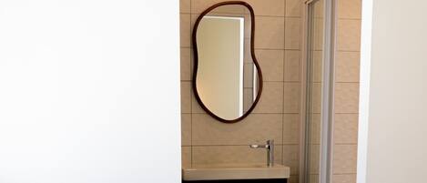 A compact hotel room with a round chair, a small sink, and a mirror.