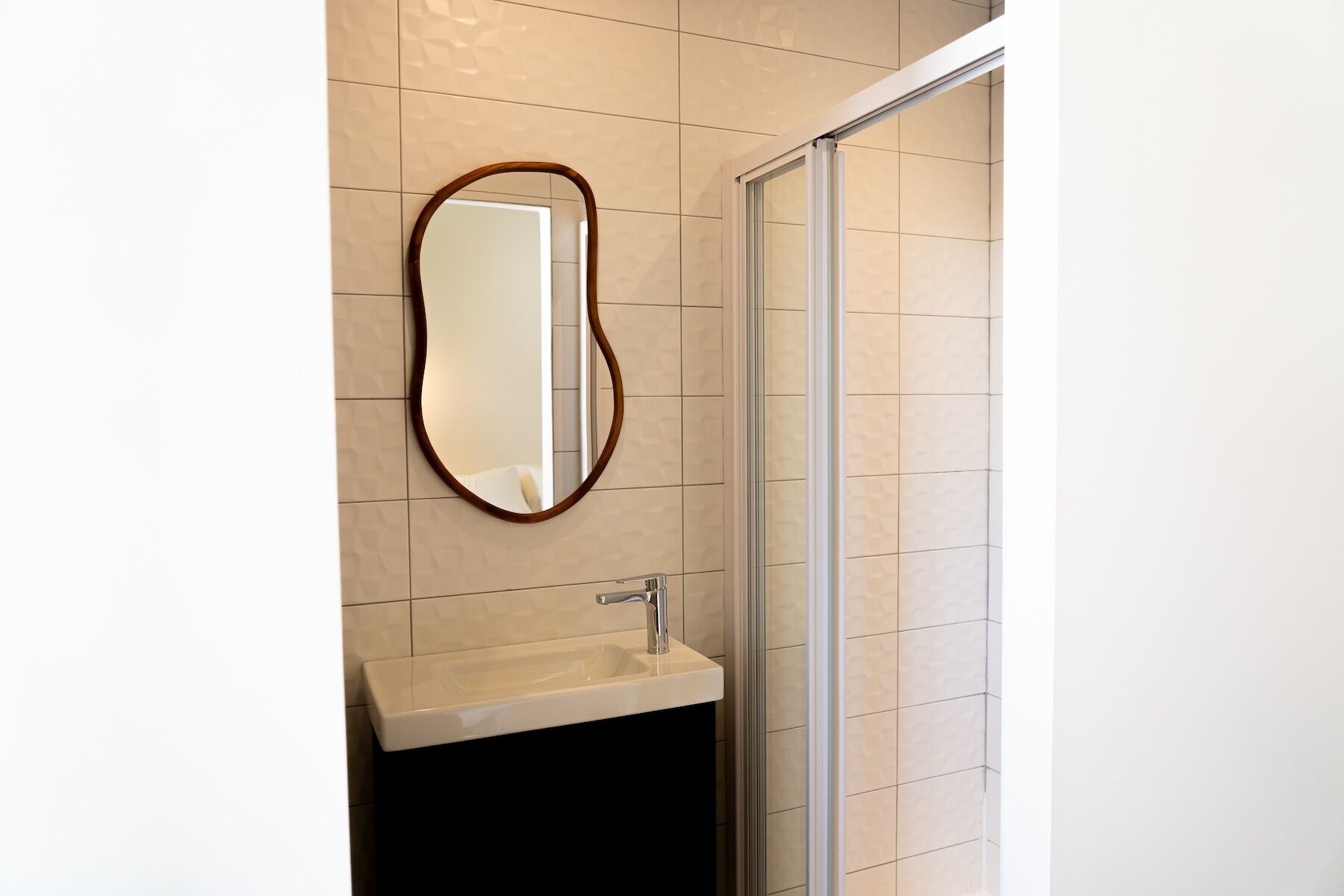 A bathroom with a mirror, sink, and shower.