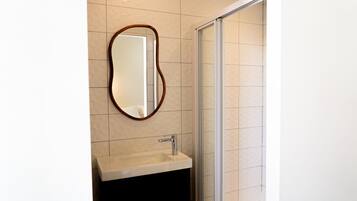 A bathroom with a mirror, sink, and shower.