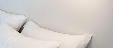 A white wall with a modern wall-mounted light fixture and two white pillows on a white sofa.