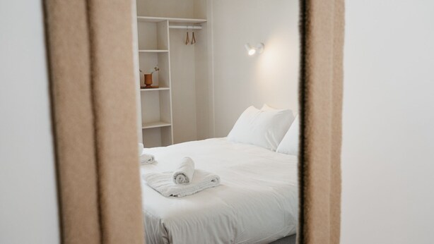 A neatly made bed with white linens and towels, a white wardrobe, and a wall-mounted light fixture. - HOTEL BLEU SOLEIL (Capbreton)