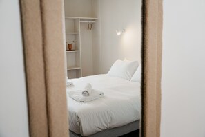 A neatly made bed with white linens and towels, a white wardrobe, and a wall-mounted light fixture. - HOTEL BLEU SOLEIL (Capbreton)