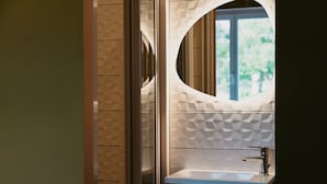 A bathroom with a modern design, featuring a round mirror, a sink, and a window with a view of greenery. - HOTEL BLEU SOLEIL (Capbreton)