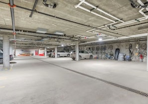 Ett underjordiskt parkeringsgarage i flera våningar med betongpelare, rör som löper längs taket och en rad parkerade bilar.