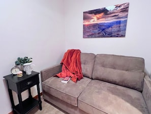 A living room with a grey sofa, a small black side table with a clock, a plant, and a magazine. - Timberline Cove Lakeside Condo • Mtn Views • Hot Tubs • Bike Path (Frisco)