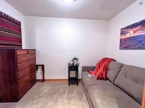 Un salon avec un canapé, une petite table sur laquelle est posée une plante, une commode en bois et un tableau accroché au mur.