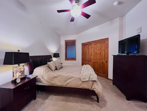 Une chambre à coucher comprenant un lit, une table de chevet, une lampe, un ventilateur de plafond, une armoire en bois et un téléviseur.