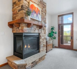 A stone fireplace with a glass door, a wooden mantel, and a painting above it. - Timberline Cove Lakeside Condo • Mtn Views • Hot Tubs • Bike Path (Frisco)