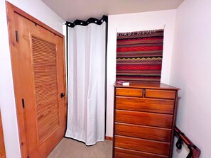 A corner room with a wooden door, a white curtain, a wooden dresser, and a patterned tapestry.