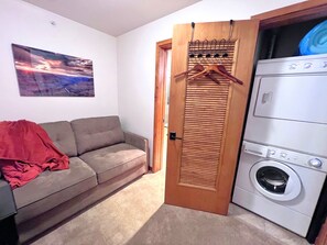A room with a grey sofa, a red blanket, a wooden door, and a washing machine.