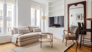 A modern living room with a sofa, a round coffee table, a television, and a large mirror. - Blueground | Gros-Caillou, view, nr Eiffel Tower (Paris)