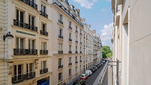 A narrow street lined with multi-story buildings, featuring balconies and a row of parked cars. - Blueground | Gros-Caillou, view, nr Eiffel Tower (Paris)