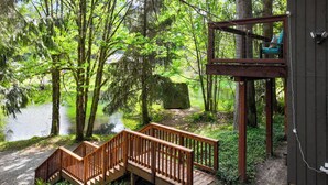 Eine Holzterrasse mit einer Treppe zu einer Plattform, von der aus ein Waldgebiet und ein Gewässer zu sehen sind.