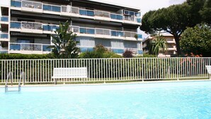 Une piscine entourée d’une clôture blanche, un banc et, au fond, un immeuble à plusieurs étages doté de balcons.
