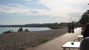 Une plage de galets, un ciel dégagé, quelques personnes et une vue lointaine sur la ville.