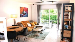 Un salon moderne avec un canapé, une table basse et une table à manger. Un tableau orne le mur et une bibliothèque est remplie de livres.