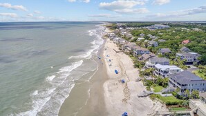 Vista aérea de una zona residencial costera con propiedades frente al mar, una playa de arena y cielo despejado.