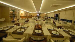 A spacious dining area with multiple tables and chairs, a central decorative piece, and a television screen. - Hotel İzgi Turhan (Batman)