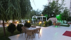 An outdoor patio with a round table and chairs, surrounded by greenery and a white pergola. - Hotel İzgi Turhan (Batman)