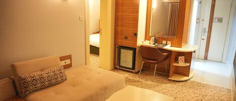 A hotel room with a sofa, a small table, a desk with a chair, a mirror, and a wardrobe.
