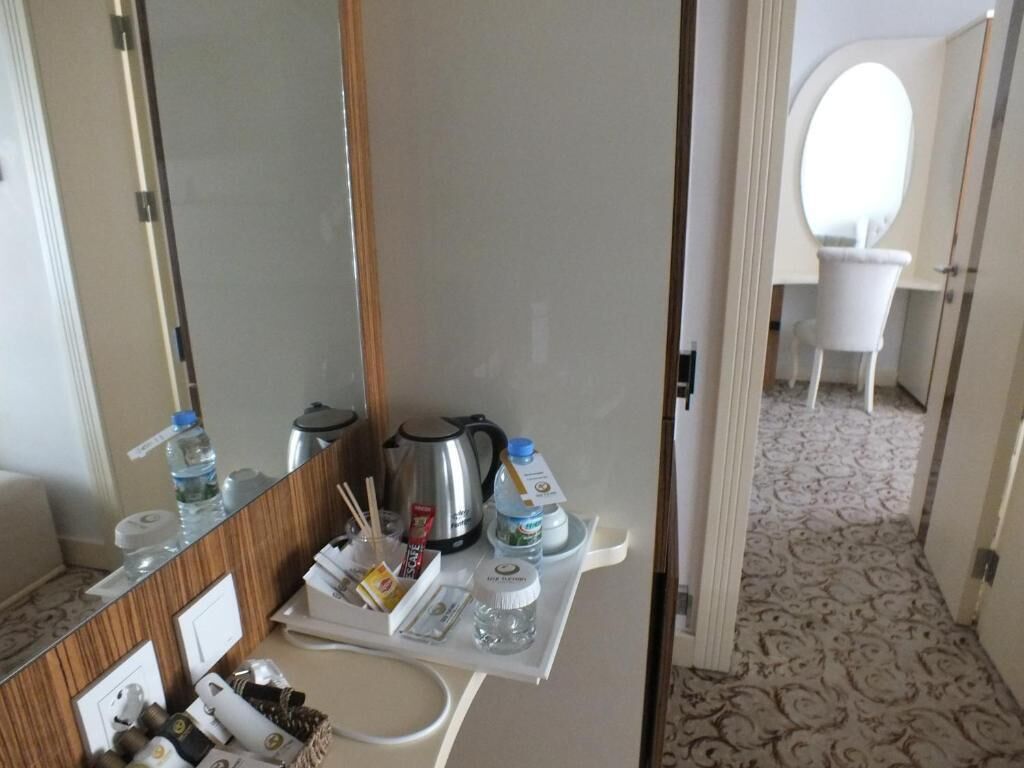 A hotel room with a minibar, a mirror, a white chair, and a patterned carpet.