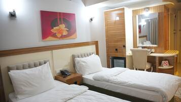 Habitación de hotel con dos camas, un escritorio, una silla, una mesita, un espejo y un cuadro en la pared.