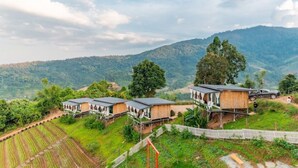 A series of wooden cabins with solar panels, set against a backdrop of lush green hills and a clear sky. - Long hug khao homestay (Pong Yaeng)
