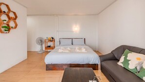 A bedroom with a bed, a bedside table, a fan, a wooden shelf, and a sofa. - Long hug khao homestay (Pong Yaeng)