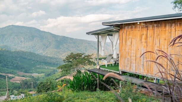 A wooden building with a covered outdoor seating area overlooking a mountainous landscape. - Long hug khao homestay (Pong Yaeng)