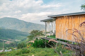 A wooden building with a covered outdoor seating area overlooking a mountainous landscape. - Long hug khao homestay (Pong Yaeng)