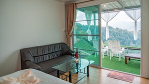 A room with a sofa, a glass table, and a view of a green landscape through large windows. - Long hug khao homestay (Pong Yaeng)