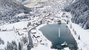 A snow-covered town with a central lake, surrounded by forested mountains.