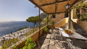 A terrace with outdoor seating, a view of the sea, and a thatched roof.