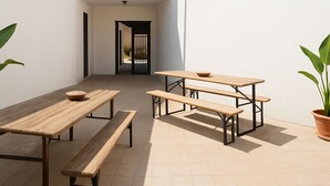An outdoor patio with wooden tables and benches, a potted plant, and a view of a building in the background. - Casa Isidoro, Ac, Seaside (Sant'isidoro)
