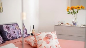 A neatly made bed with floral pillows, a bottle, and rolled towels on a white bedspread. - Casa Isidoro, Ac, Seaside (Sant'isidoro)