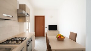 A modern kitchen with a gas stove, oven, and a dining table with a fruit basket. - Casa Isidoro, Ac, Seaside (Sant'isidoro)