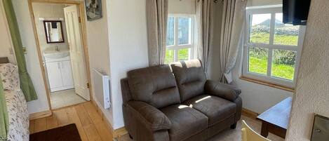 Ein gemütliches Wohnzimmer mit einem braunen Sofa, einem kleinen Tisch und einem Fenster mit Vorhängen.