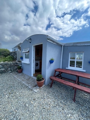 A small building with a stone wall, a washing machine, and a bench. - Calla By the Sea (Roundstone)
