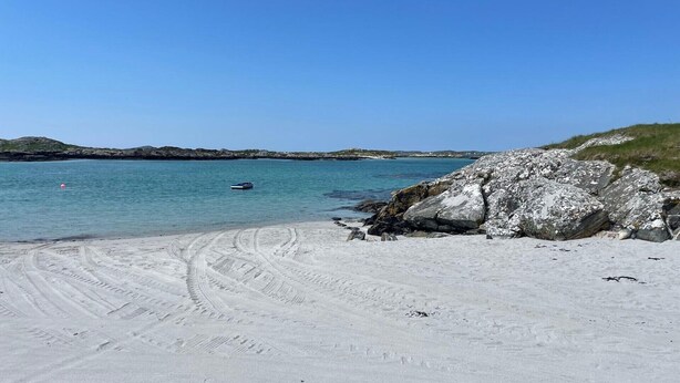 A sandy beach with tire tracks leading to the water, a large rock formation, and a small boat in the distance. - Calla Chalet by the Sea Roundstone (Roundstone)