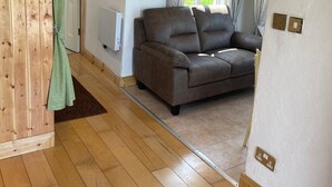 A cozy room with a wooden floor, a brown sofa, a green curtain, and a window with curtains. - Calla Chalet by the Sea Roundstone (Roundstone)