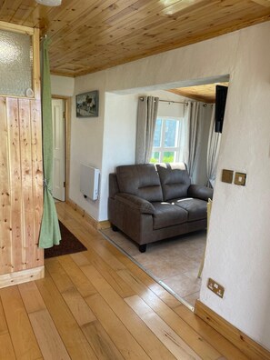 A room with a wooden floor, a brown sofa, a green curtain, and a window with curtains.
