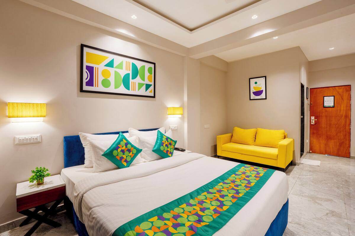 Una habitación de hotel con una cama, un sillón amarillo y obras de arte en las paredes.