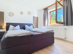 Un dormitori modern amb un llit gran, dues taules de nit, una finestra amb cortines i un radiador.