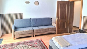 A room with a grey sofa, a wooden door, and a bed with a white blanket.