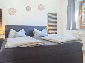 Una cama doble con dos almohadas, una mesita de noche con una lámpara y tres relojes en la pared.
